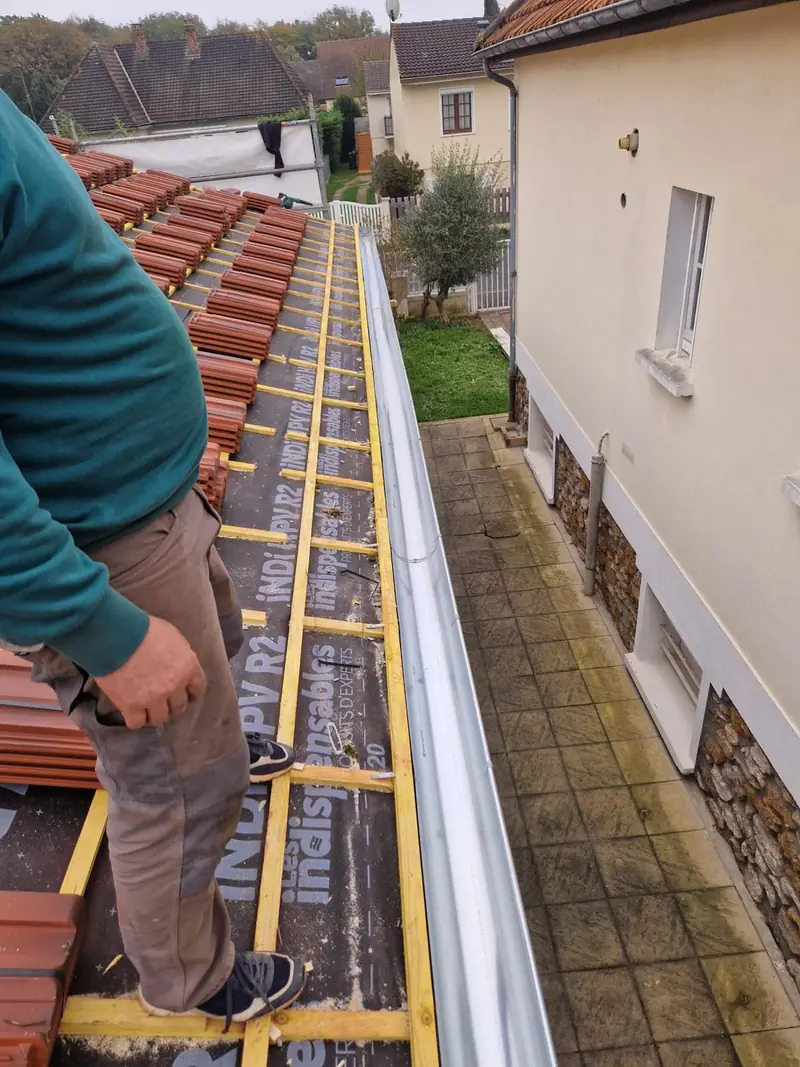 Couvreur sur le litelage avec gouttière neuve et tuiles prêtes à poser par Les Toitures de Kevin, couvreur en Essonne