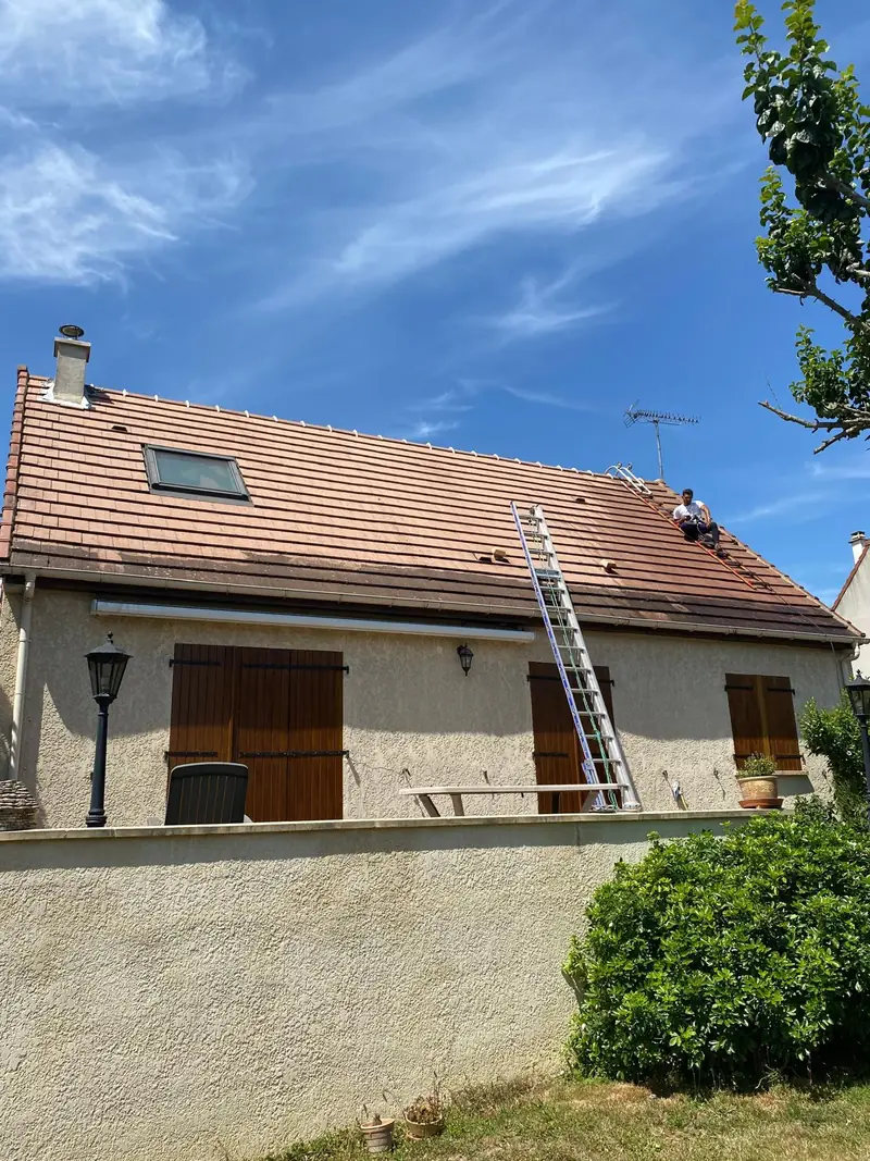Couvreur intervenant sur une toiture avec fenêtre de toit pour son nettoyage par Les Toitures de Kevin, couvreur en Essonne