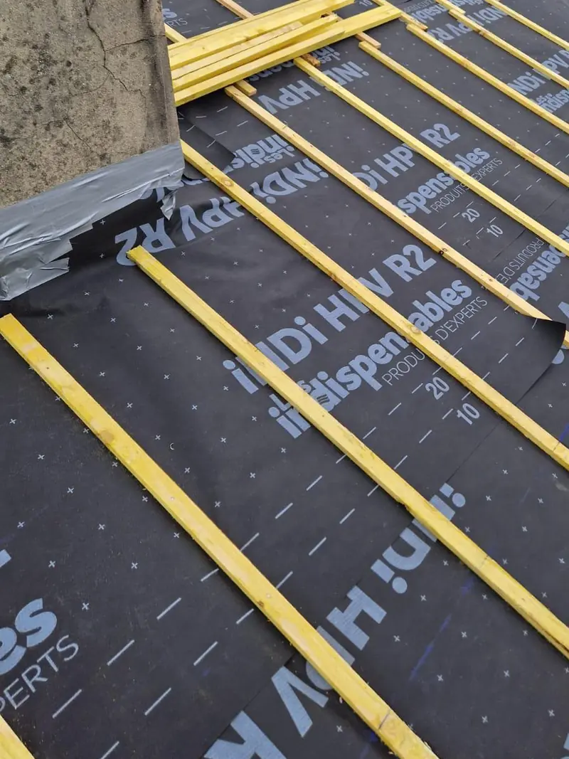 Écran souple de sous-toiture noir posé sur un pan de toit, avec des liteaux neufs fixés et un paquet de liteaux en attente
